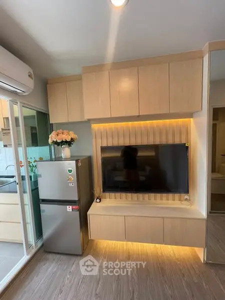 Modern living room with sleek cabinetry and mounted TV, featuring a compact kitchen area with stainless steel fridge.