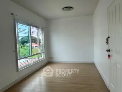 Bright empty room with large window and wooden flooring, perfect for customization.