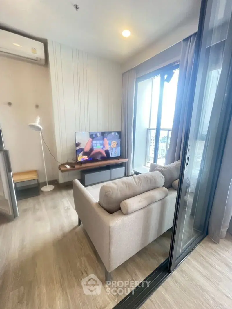 Modern living room with cozy sofa and TV, featuring large windows and balcony access.