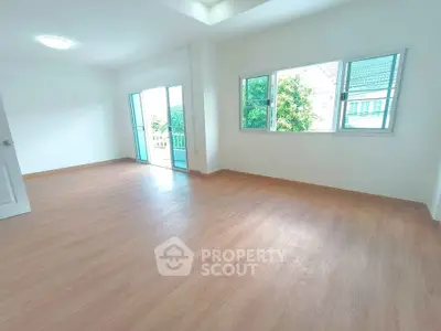 Spacious empty room with wooden flooring and large windows offering natural light.