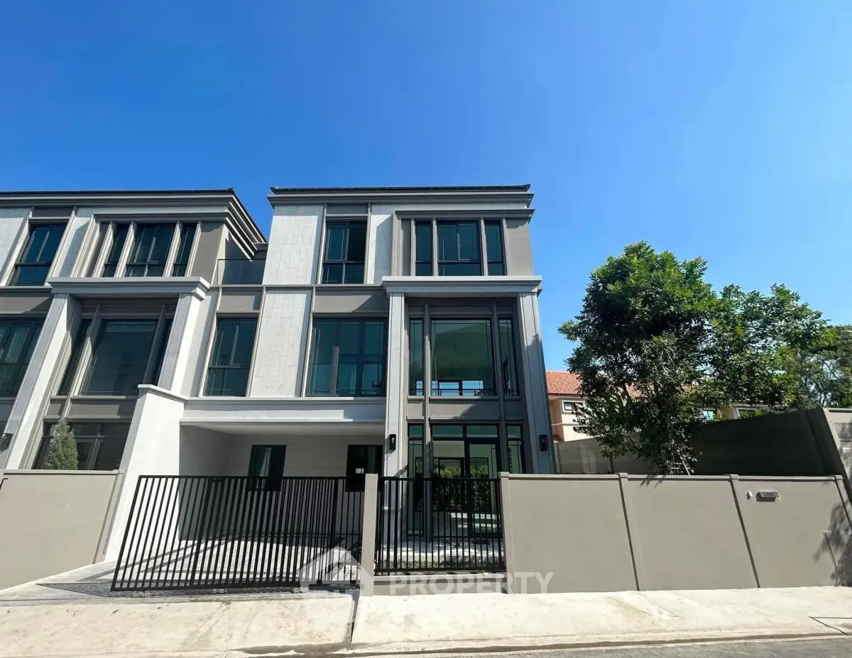 Modern three-story townhouse with sleek design and gated entrance under clear blue sky.
