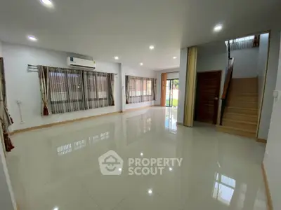 Spacious modern living room with large windows and staircase in a stylish home.