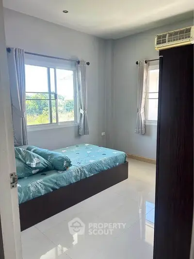Bright bedroom with large windows and modern air conditioning unit, offering a serene view.