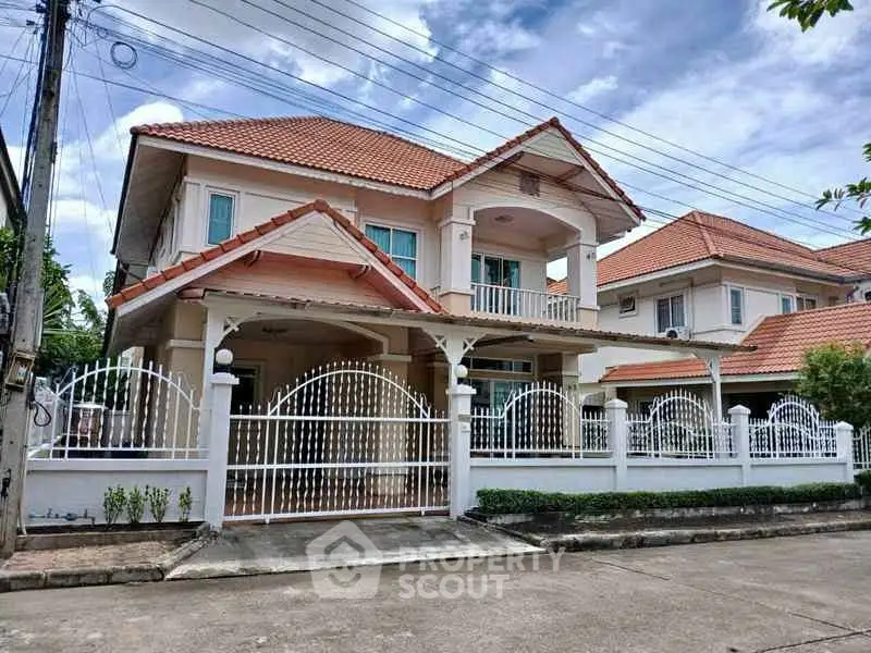 Charming two-story house with red-tiled roof and white fence in a serene neighborhood.