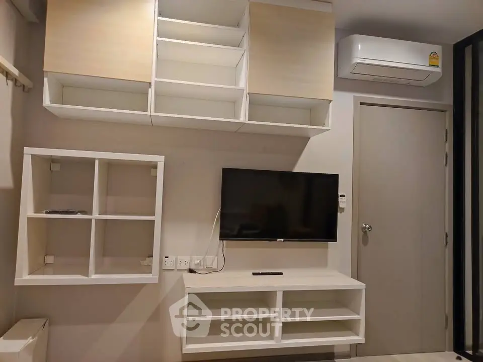 Modern living room with wall-mounted TV and air conditioning unit, featuring sleek storage solutions.