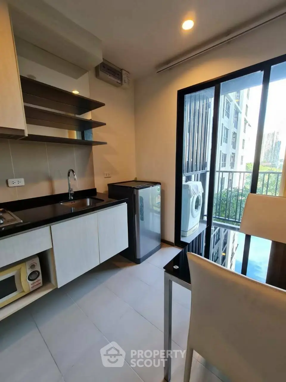 Modern kitchen with sleek cabinetry, compact fridge, and washing machine in a bright apartment.