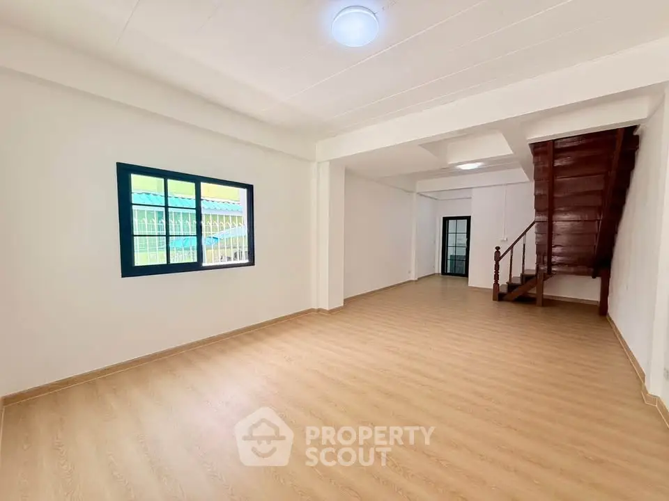 Spacious open-plan living room with wooden staircase and bright window view.