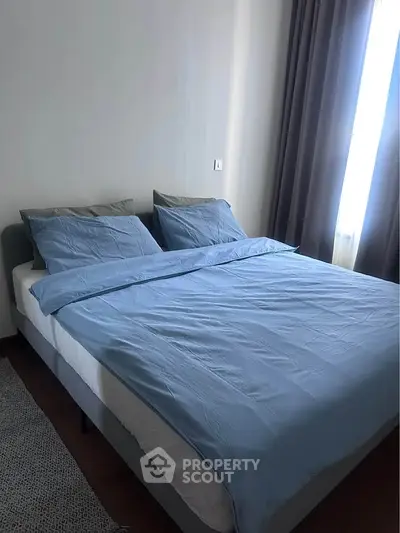 Cozy bedroom with elegant blue bedding and natural light from large window.