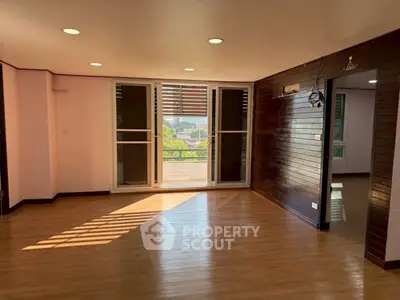 Spacious living room with large windows and wooden flooring, offering abundant natural light.