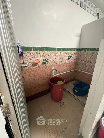 Simple bathroom with tiled walls and floor, featuring a bucket and basic fixtures.