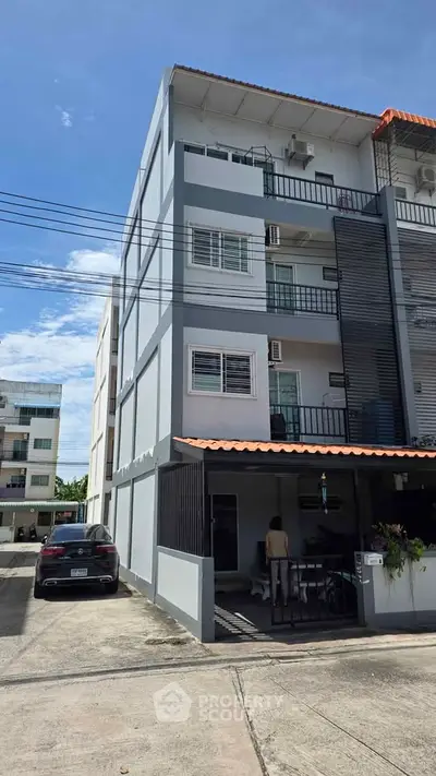 Modern multi-story residential building with parking area and clear blue sky.