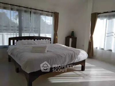 Spacious bedroom with large windows and natural light, featuring a cozy bed and elegant curtains.