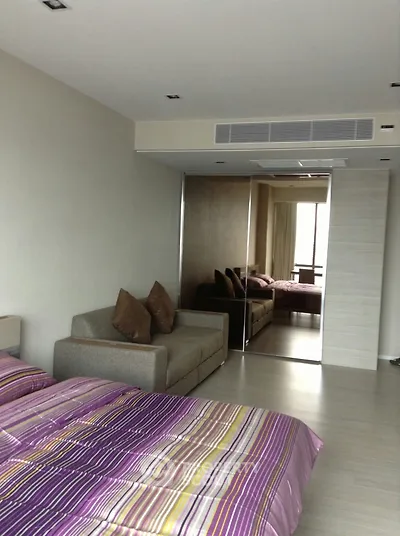 Spacious bedroom with mirrored closet and cozy seating area in modern apartment.