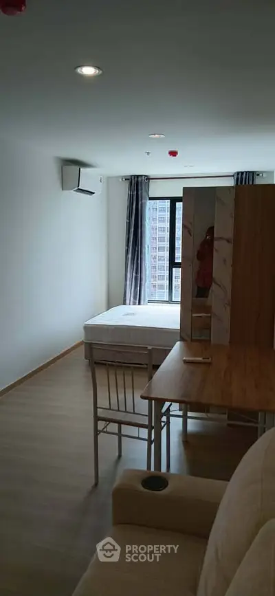 Modern bedroom with large window and wooden furniture in a high-rise apartment.