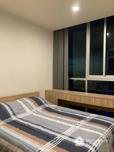 Modern bedroom with large window offering stunning city view, featuring a cozy bed and sleek wooden furniture.