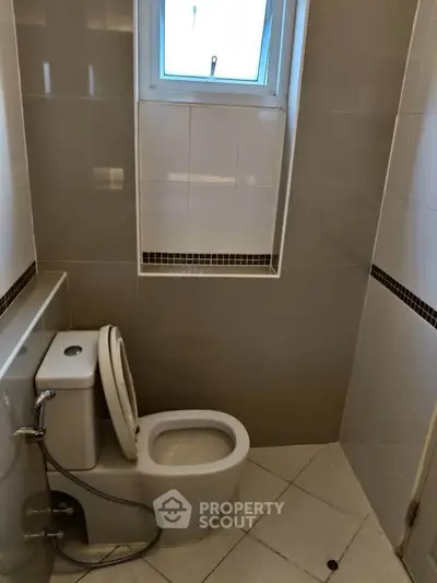 Compact bathroom with modern toilet and tiled walls, featuring a small window for natural light.