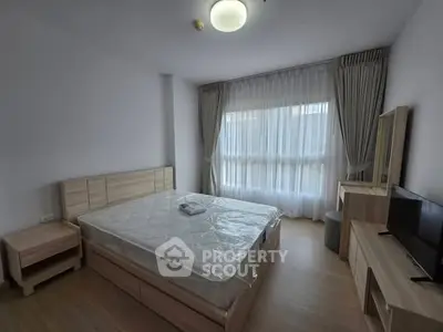 Spacious bedroom with large window and modern furnishings in a well-lit apartment.