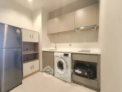 Modern kitchen with sleek appliances and ample storage space, featuring a washing machine and stainless steel fridge.