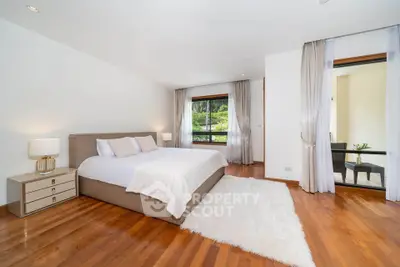 Spacious modern bedroom with hardwood floors and large windows offering scenic views.