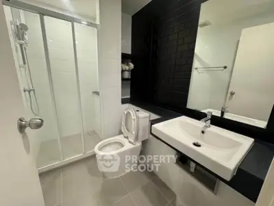 Modern bathroom with sleek black and white design, featuring a shower, toilet, and stylish sink.