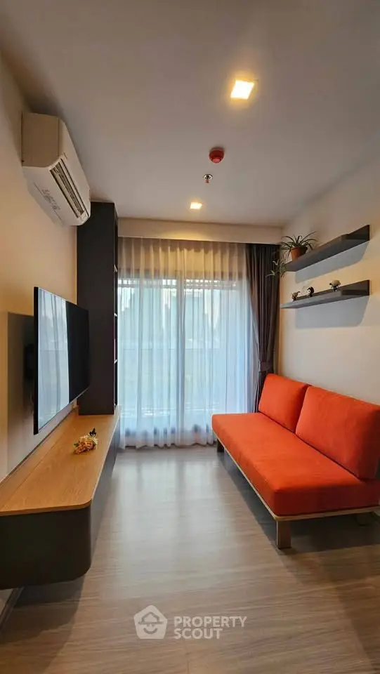 Modern living room with orange sofa, wall-mounted TV, and large window with sheer curtains.