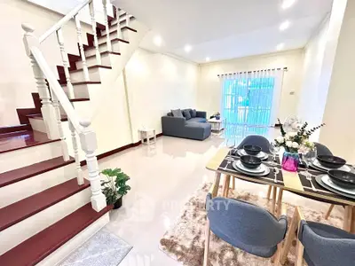 Spacious living room with elegant staircase and dining area, featuring modern decor and natural lighting.