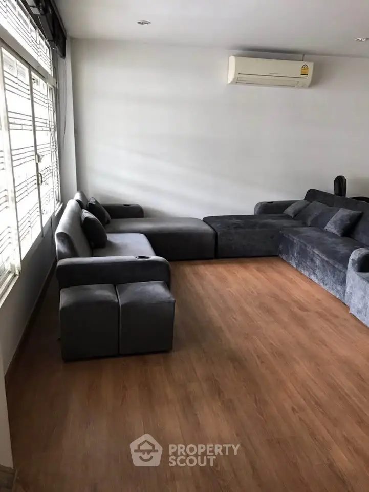Spacious living room with modern gray sofas and wooden flooring, featuring ample natural light from large windows.
