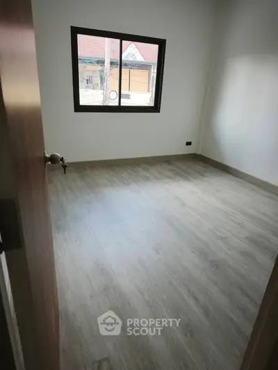 Spacious empty room with wooden flooring and large window, ideal for customization.