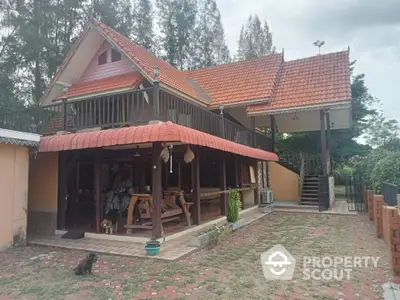 Charming traditional-style home with terracotta roof tiles, expansive paved courtyard, and a cozy outdoor seating area under a covered porch, surrounded by lush greenery.