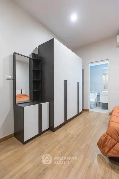 Modern bedroom with sleek wardrobe and ensuite bathroom, featuring wooden flooring and contemporary design.