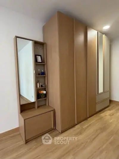 Modern bedroom with sleek wooden wardrobe and vanity mirror, showcasing minimalist design and ample storage space.