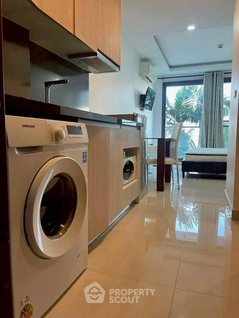 Modern apartment interior with sleek kitchen and washing machine, featuring a bright living area with large windows.