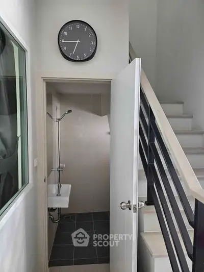 Compact bathroom under staircase with modern design and wall clock
