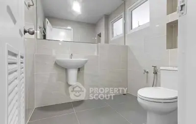 Modern bathroom with sleek fixtures and neutral tiles, featuring a wall-mounted sink and toilet.
