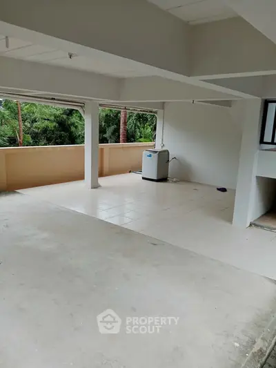 Spacious balcony with washing machine and lush green view, perfect for relaxation and utility.
