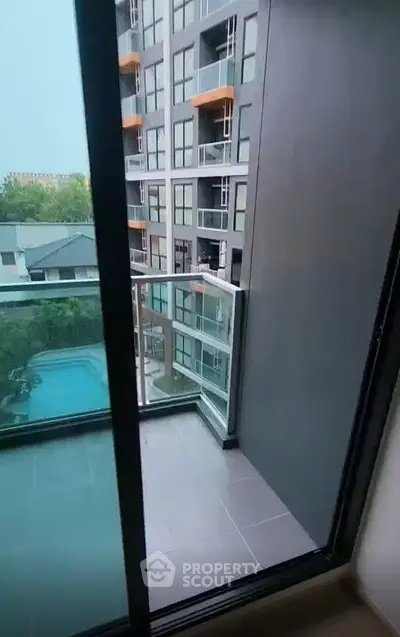 Modern apartment balcony with glass railing overlooking pool and neighboring building.