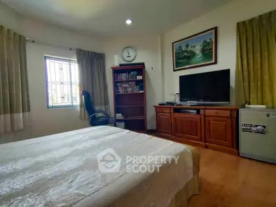 Cozy bedroom with TV, bookshelf, and window view in a stylish home.