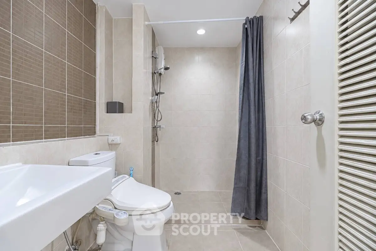 Modern bathroom with sleek design and neutral tiles, featuring a shower and toilet.