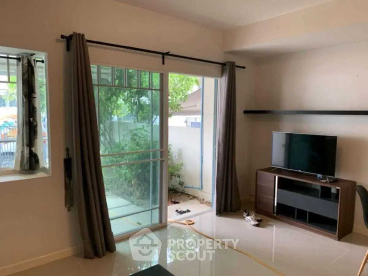 Cozy living room with sliding glass doors leading to a small garden area, featuring a TV and modern decor.