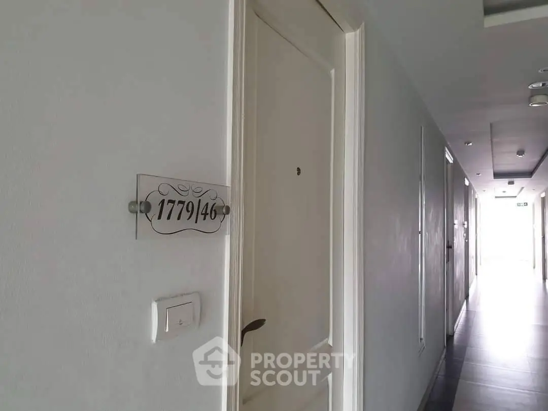 Modern apartment hallway with white door and room number plaque.