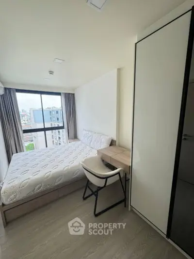 Modern bedroom with city view, featuring sleek furniture and large window for natural light.
