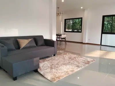 Spacious modern living room with sleek gray sofa and plush rug, featuring large windows for natural light.