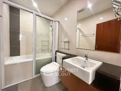 Modern bathroom with sleek fixtures and glass-enclosed bathtub in contemporary apartment.