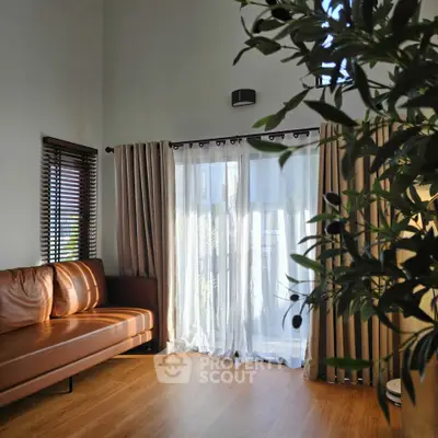 Bright living room with leather sofa and large window draped with curtains