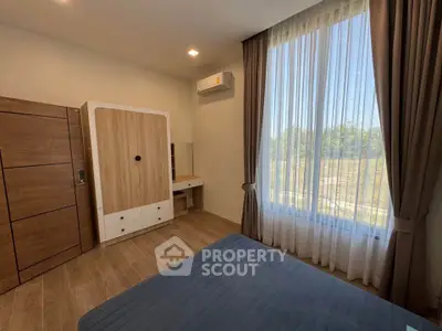 Modern bedroom with large window and wooden furniture, offering a serene view.