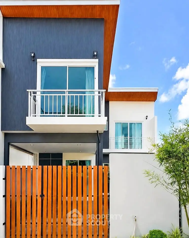 Modern two-story house with sleek design and small balcony, featuring wooden accents and large windows.