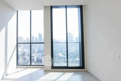 Bright empty room with floor-to-ceiling windows offering stunning city skyline views.