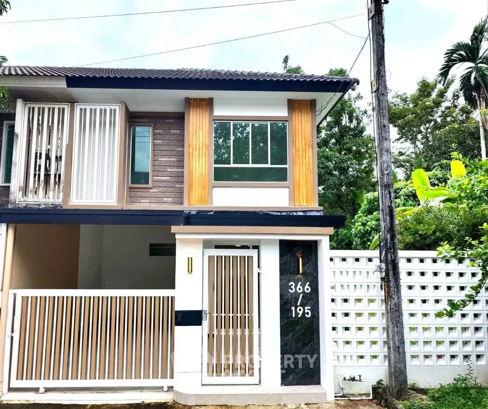 Modern two-story house with stylish facade and gated entrance in lush green setting.