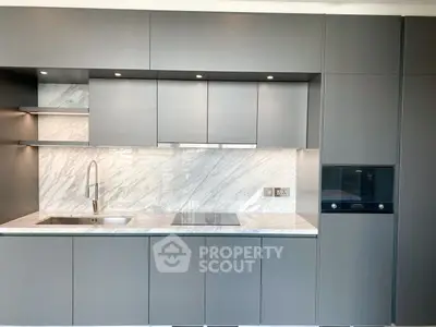Modern kitchen with sleek gray cabinets and marble backsplash, featuring built-in oven and induction cooktop.