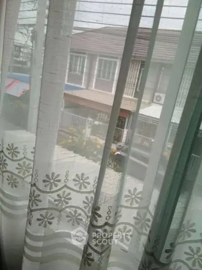 Charming residential view through elegant floral curtains, showcasing a peaceful neighborhood scene.